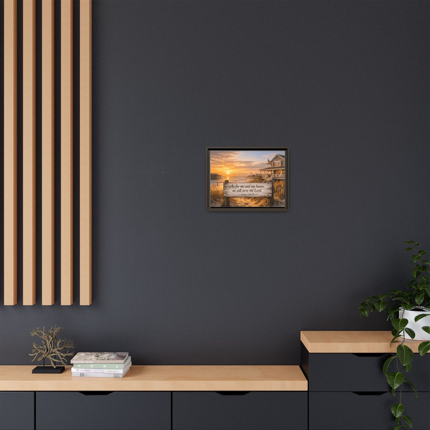 Framed coastal scripture wall art on dark wall above console with plants and decor.