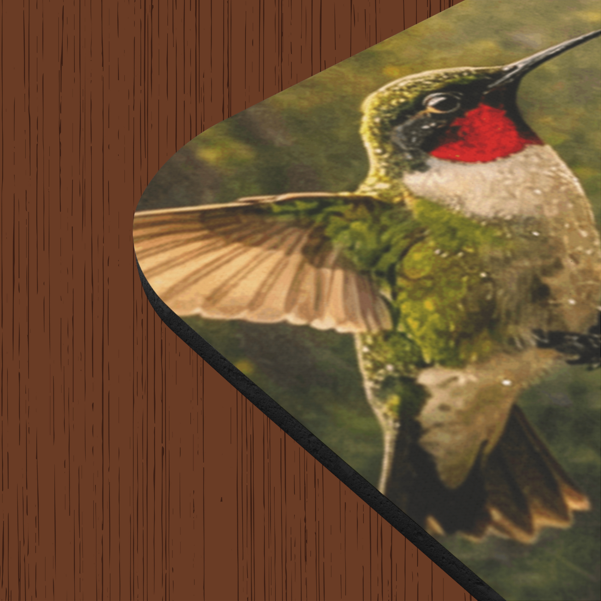 A close-up of a printed mouse pad or desk mat showing a hummingbird in flight, placed on a brown wood-grain surface. The bird has green, white, and red coloring, with blurred wings in beige tones. The corners are rounded and shows thickness of the mouse pad.
