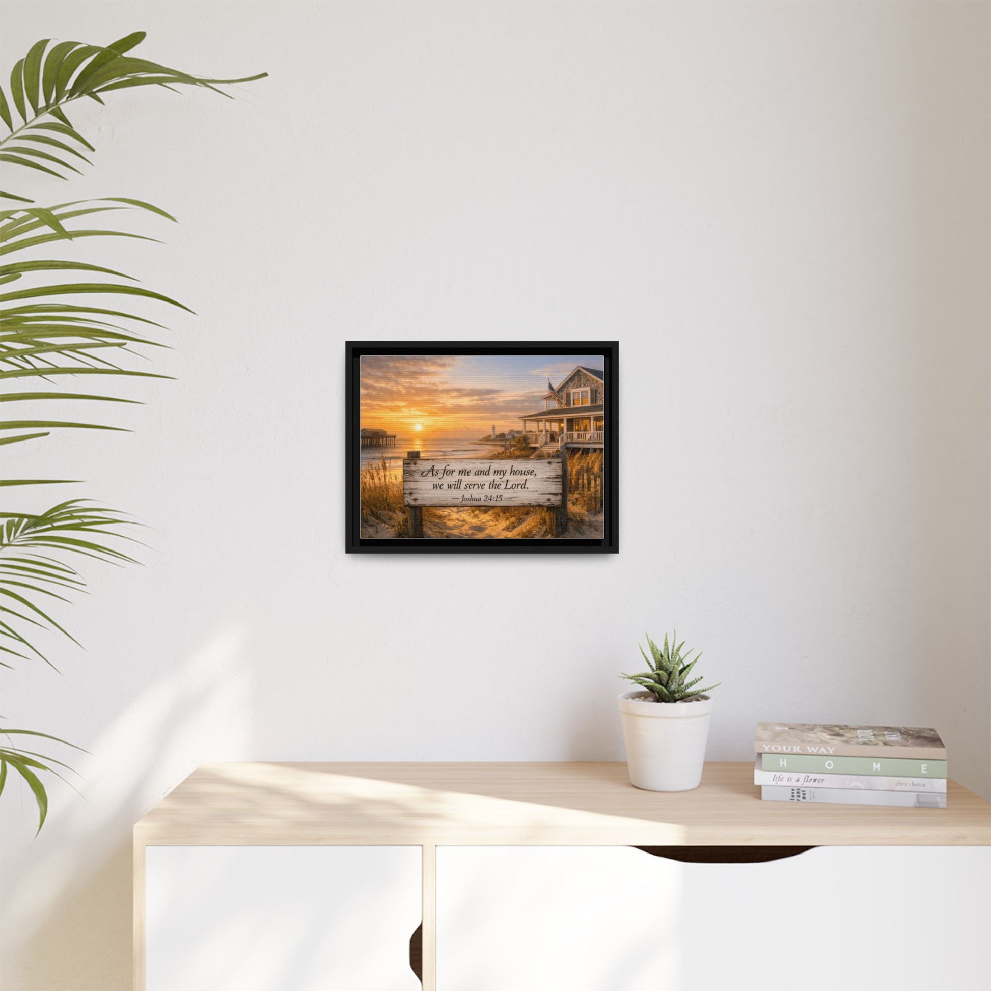 Small framed coastal scripture wall art on white wall with potted plant and books.