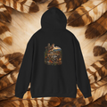 A black pullover hoodie shown from the back, featuring a large graphic print with a hawk, mountain, and the text 'I'm Praying For You.' The hoodie is laid flat on a background of brown and tan feathers.