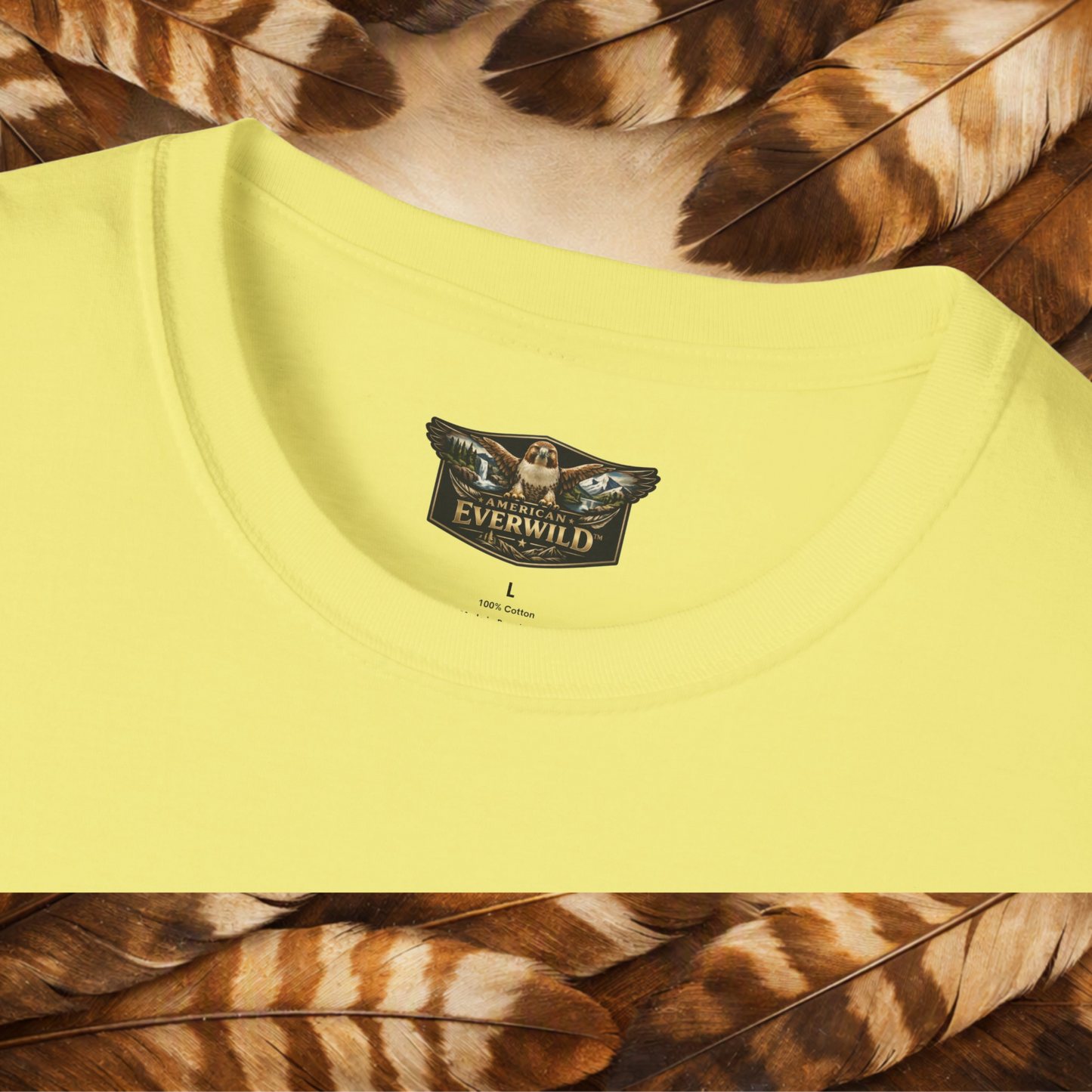 A close-up of a pale yellow t-shirt showing the inner neck label with the 'American Everwild' brand logo, styled with brown and tan feathers at the top and bottom.