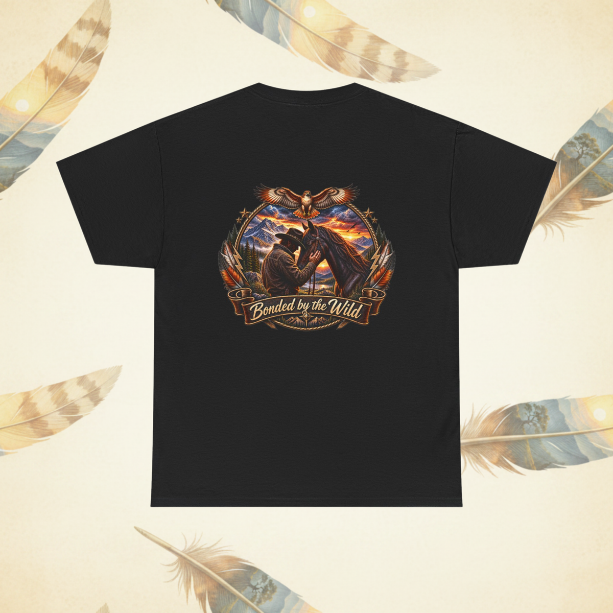 A black crew neck t-shirt viewed from the back with a horse and man with mountains and sunset graphic with the words "Bonded by the Wild" below it laid flat on a cream background with large scenic feathers.