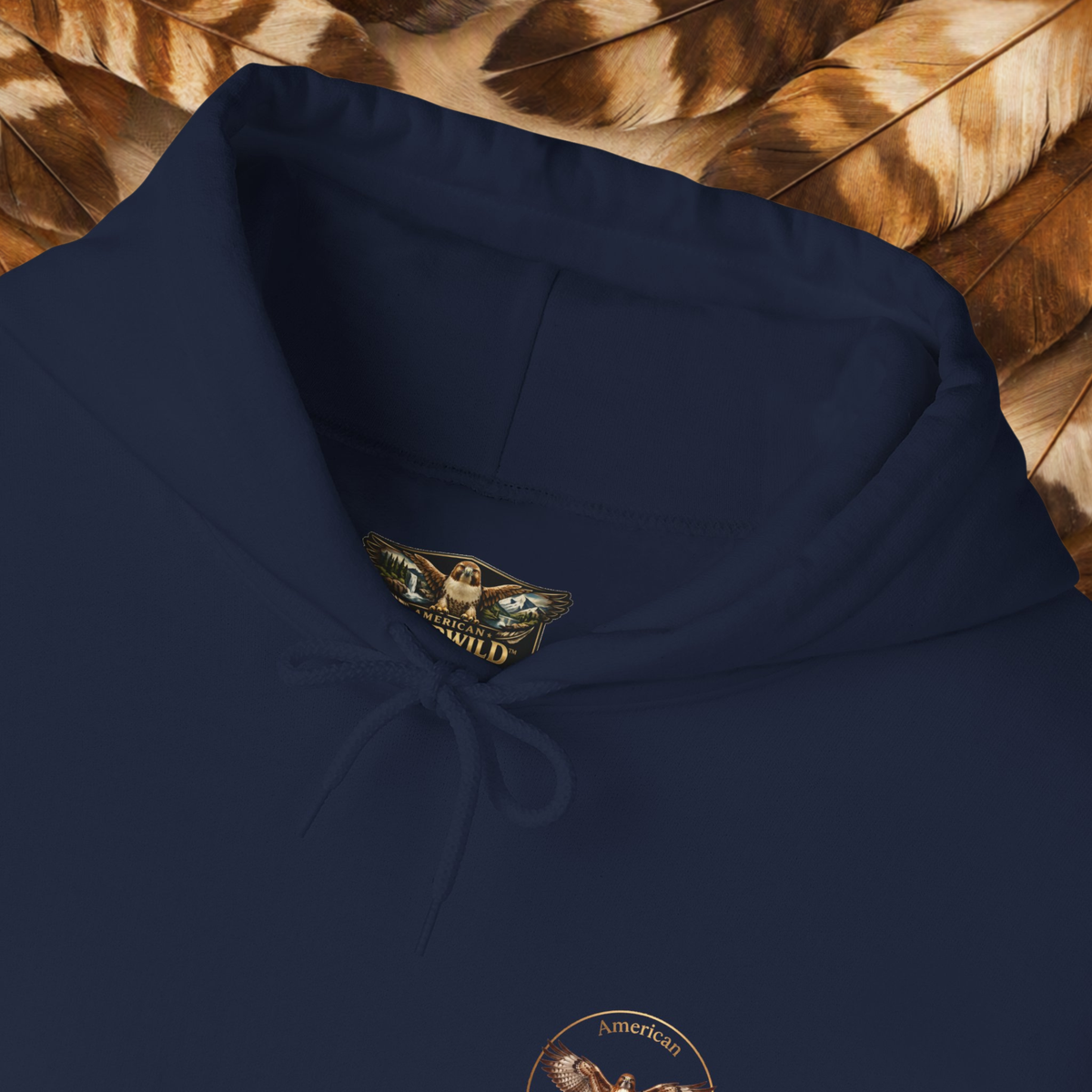 Navy Hoodie with close up of the collar hawk American EverWild logo on a backround of brown and cream feathers.