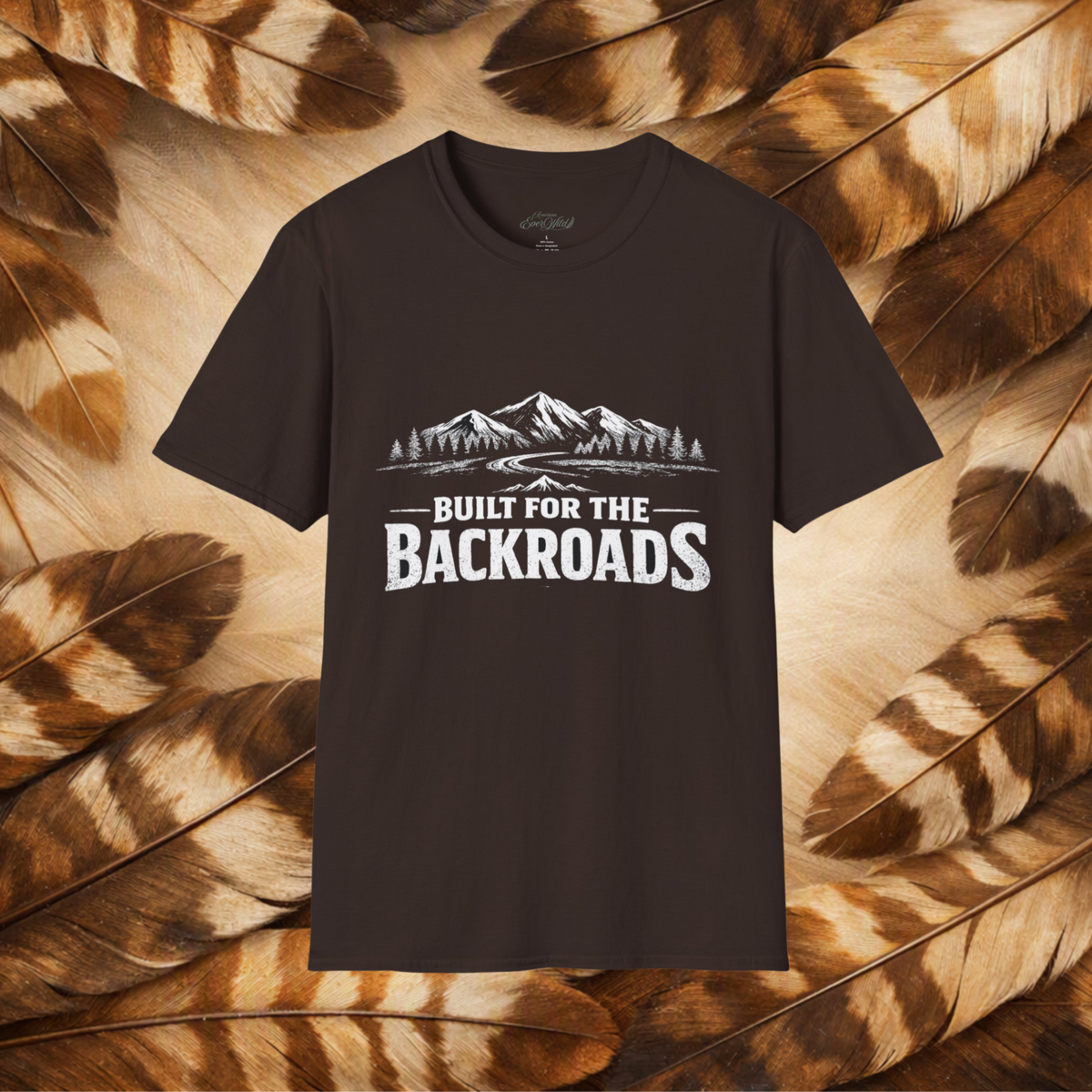A dark brown short-sleeve t-shirt with a white graphic print of mountains and the text 'BUILT FOR THE BACKROADS' displayed against a background of brown and beige feathers.