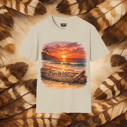 A sand color tee with a graphi of a sunset over the beach and a drift log with carved text 'EverWild—Drift Easy-Live wild' and feather quill leaning on the log in the sand. Flat lay on a background of tan and brown feathers.