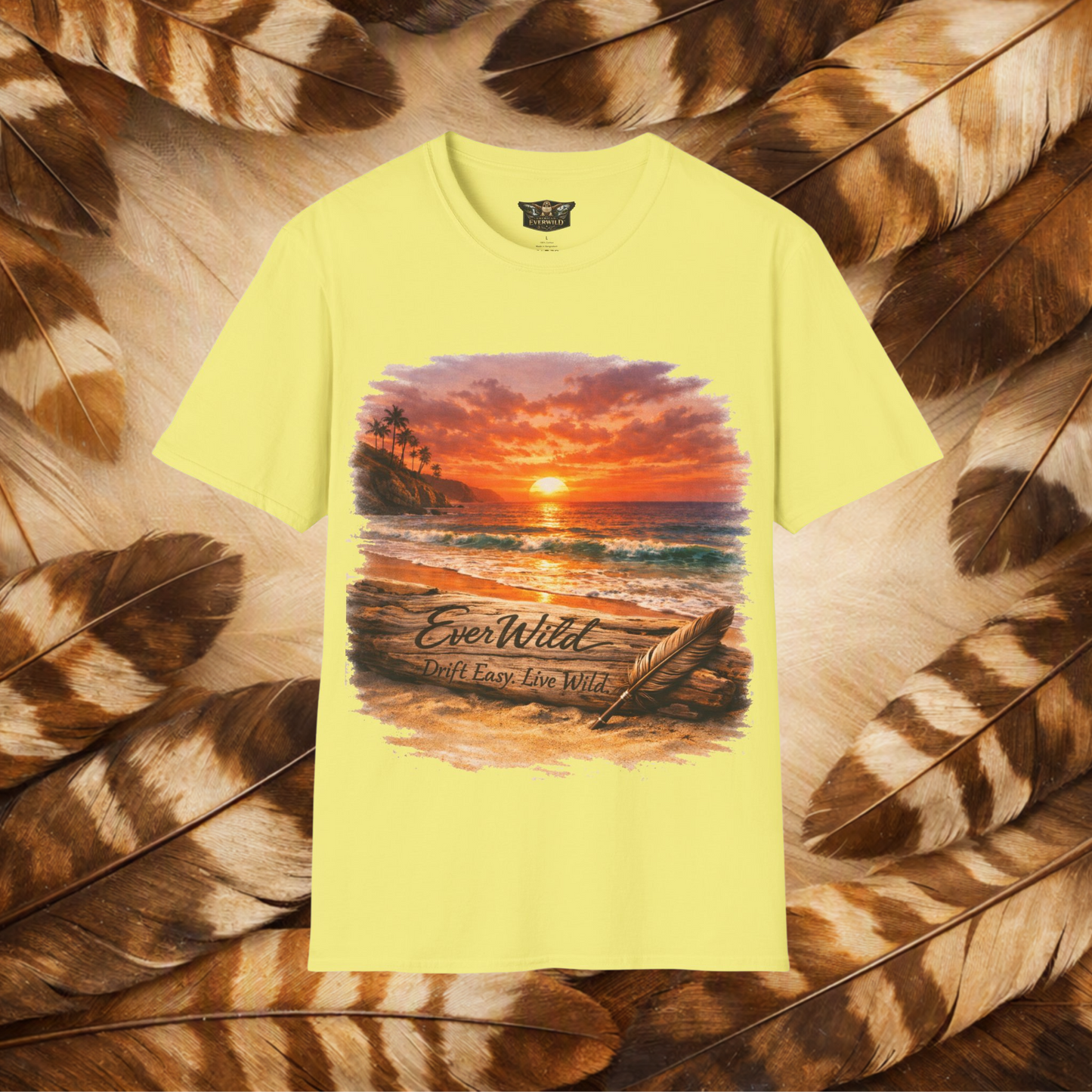 A pale yellow short-sleeve t-shirt with a colorful graphic of a beach sunset and the text 'EverWild Drift Easy-Live Wild', presented on a background of brown and tan feathers.