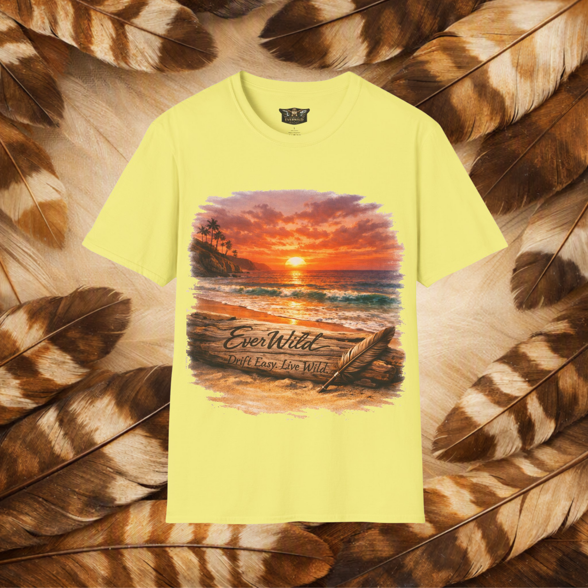 A pale yellow short-sleeve t-shirt with a colorful graphic of a beach sunset and the text 'EverWild Drift Easy-Live Wild', presented on a background of brown and tan feathers.