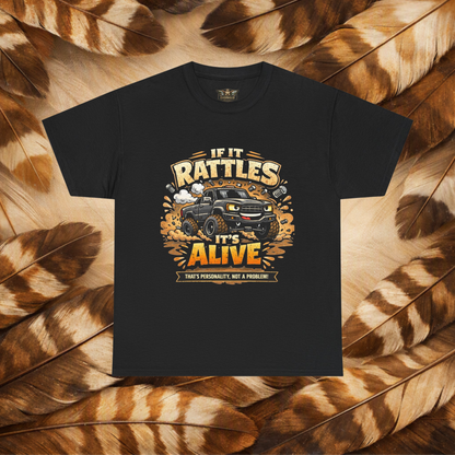 A black short-sleeve graphic t-shirt laid flat on a background of Hawk feathers. The graphic features a cartoon truck surrounded by text that reads 'IF IT RATTLES IT'S ALIVE' and 'THAT'S PERSONALITY, NOT A PROBLEM'.