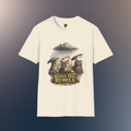 An natural short-sleeve crewneck t-shirt featuring a graphic print of three forest animals holding umbrellas under a rainy storm cloud, with the text 'RAINY DAY REBELS' below them, on a hawk feather flat lay background.