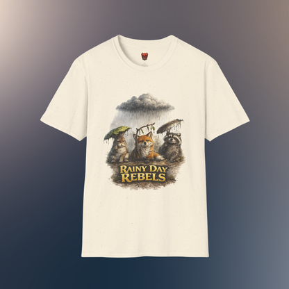 An natural short-sleeve crewneck t-shirt featuring a graphic print of three forest animals holding umbrellas under a rainy storm cloud, with the text 'RAINY DAY REBELS' below them, on a hawk feather flat lay background.