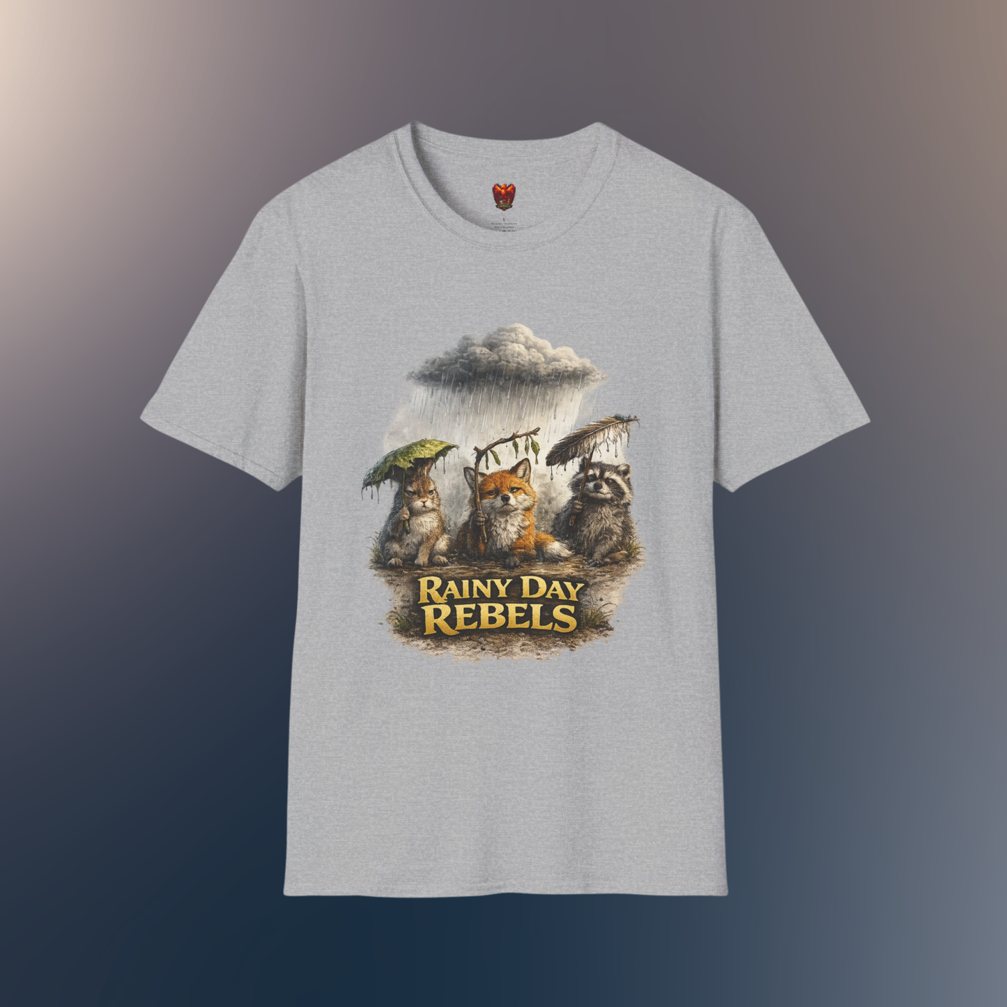 A light gray heather crewneck t-shirt featuring a graphic print of three forest animals holding umbrellas under a rainy storm cloud, with the text 'Rainy Day Rebels' below them, on a hawk feather flat lay background.