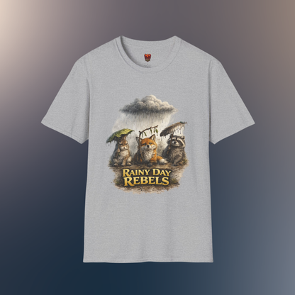 A light gray heather crewneck t-shirt featuring a graphic print of three forest animals holding umbrellas under a rainy storm cloud, with the text 'Rainy Day Rebels' below them, on a hawk feather flat lay background.