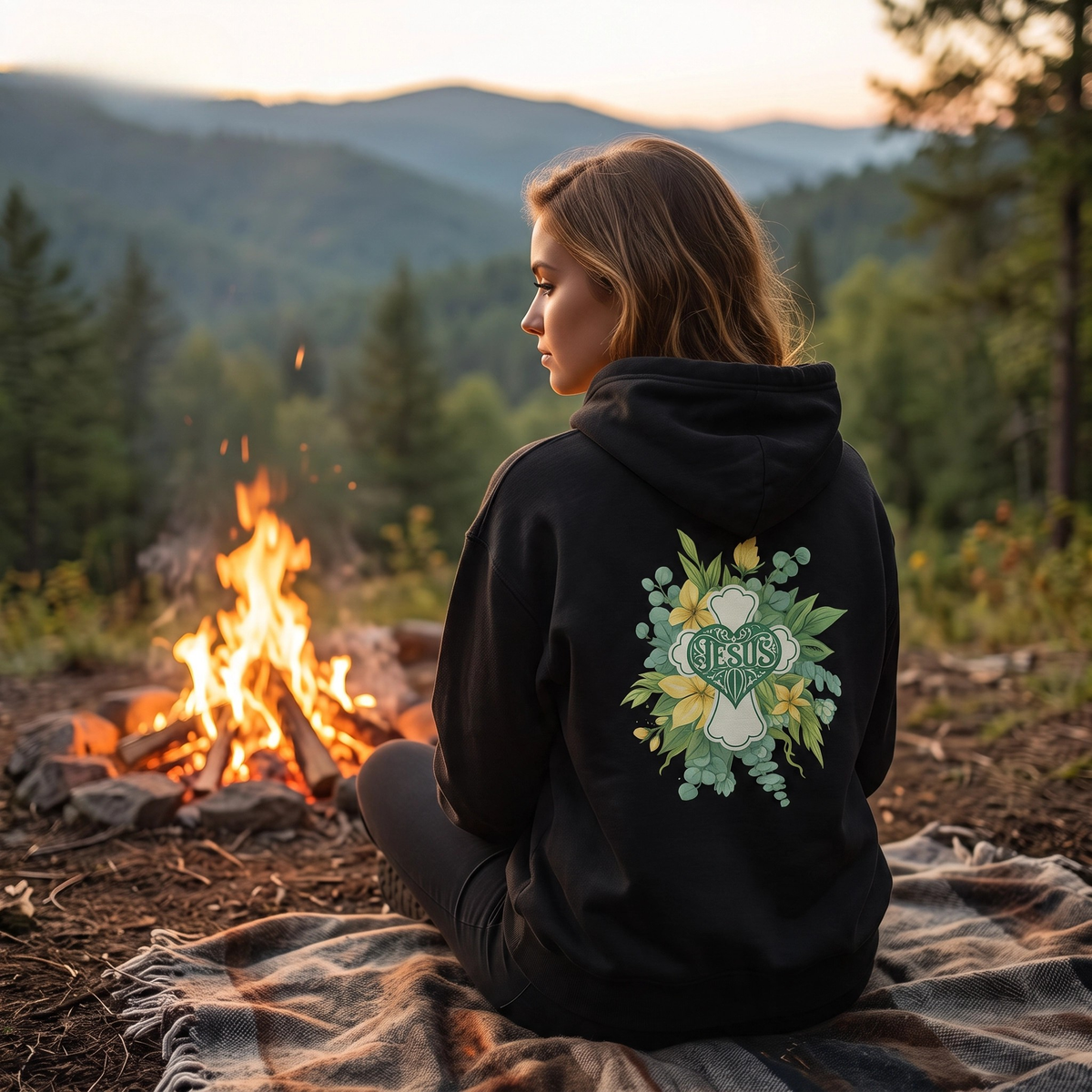 Black hooded sweatshirt with floral Jesus graphic on back, sitting outdoors