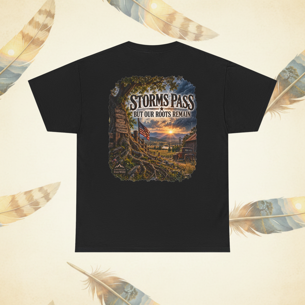 A black short-sleeve t-shirt with a large graphic print on the back, featuring a scenic 'Storms Pass' landscape with the text 'But Our Roots Remain'. The t-shirt is displayed flat against a cream-colored background decorated with feather illustrations.