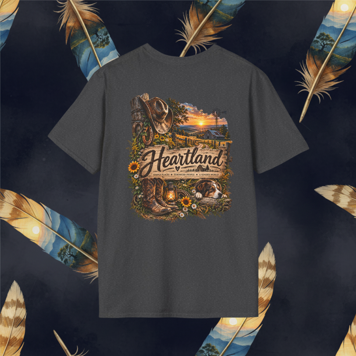 A dark charcoal gray t-shirt featuring a detailed 'Heartland' country-themed graphic print on the front, displayed against a dark background decorated with large decorative feathers.