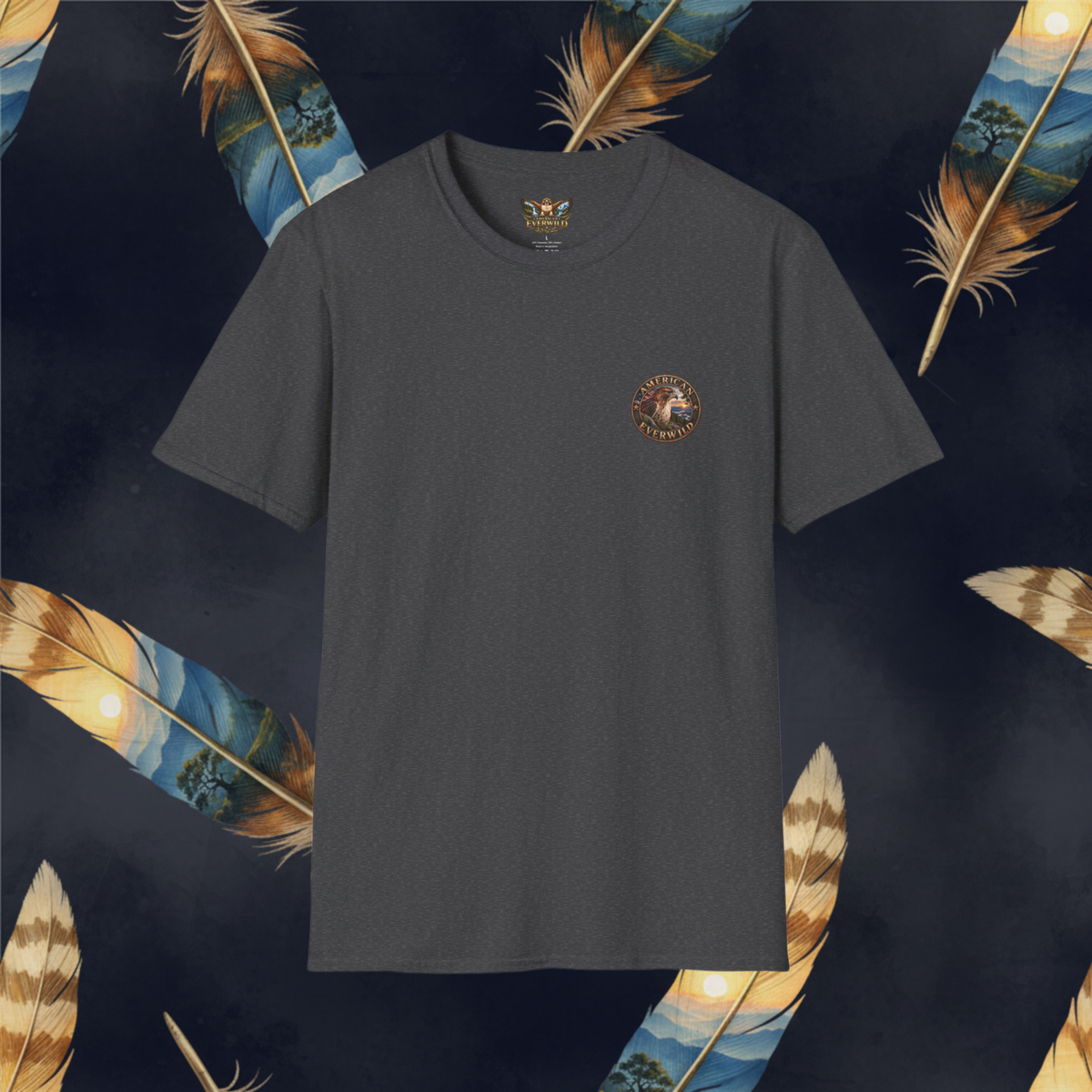 A dark charcoal gray crewneck t-shirt with a small circular graphic on the left chest, displayed against a dark navy background decorated with large golden-brown feathers.