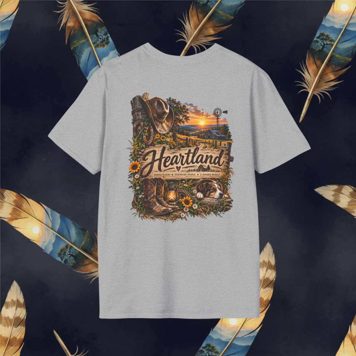 A light gray heather crewneck t-shirt featuring a detailed western-themed graphic print with the text 'Heartland'  displayed against a dark background decorated with large golden feathers.