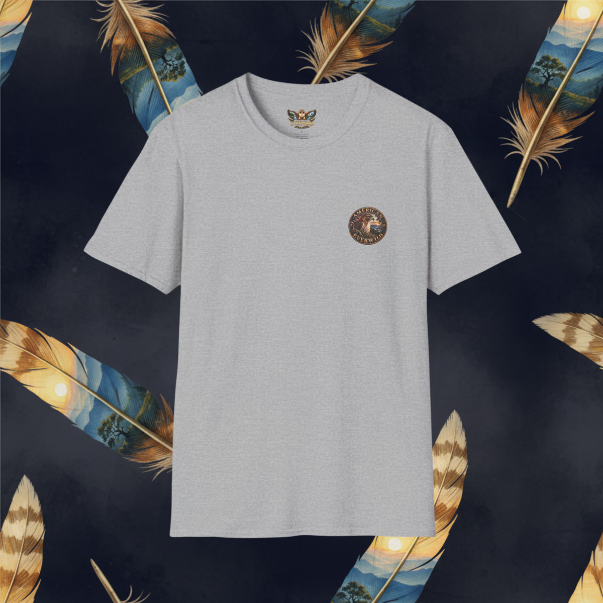 A light gray crewneck t-shirt with a small circular graphic on the left chest, displayed against a dark background decorated with golden and blue feathers.