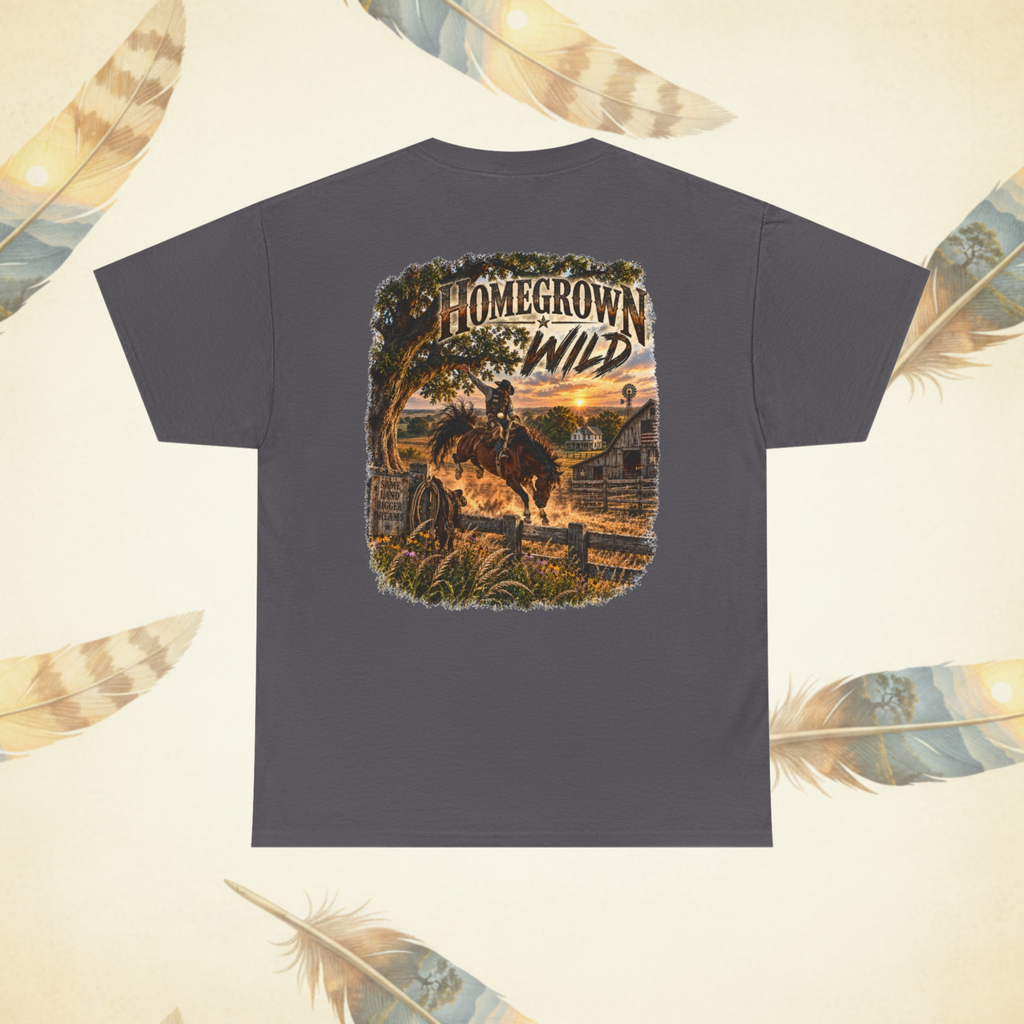 A dark gray t-shirt shown from the back, featuring a large graphic print of a cowboy riding a horse through a rustic western landscape at sunset with the text 'HOMEGROWN WILD'. The t-shirt is displayed against a light cream background decorated with scattered feather illustrations.