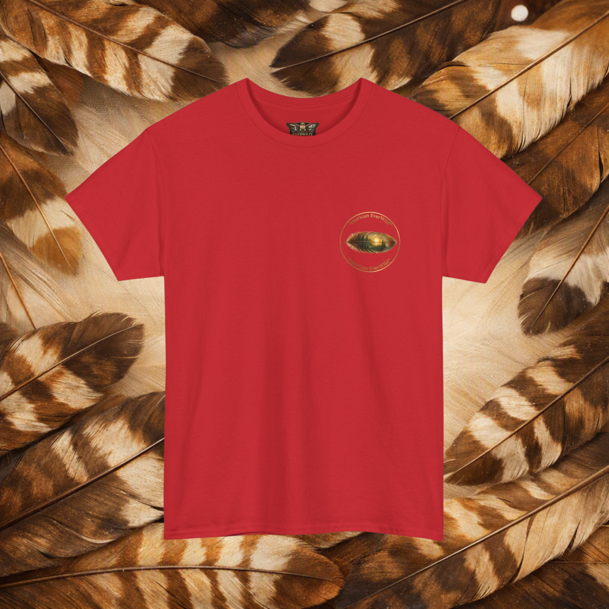 A red short-sleeve crewneck t-shirt with a small circular American EverWild name top and bottom with a painted feather, displayed flat against a background of brown and beige feathers.