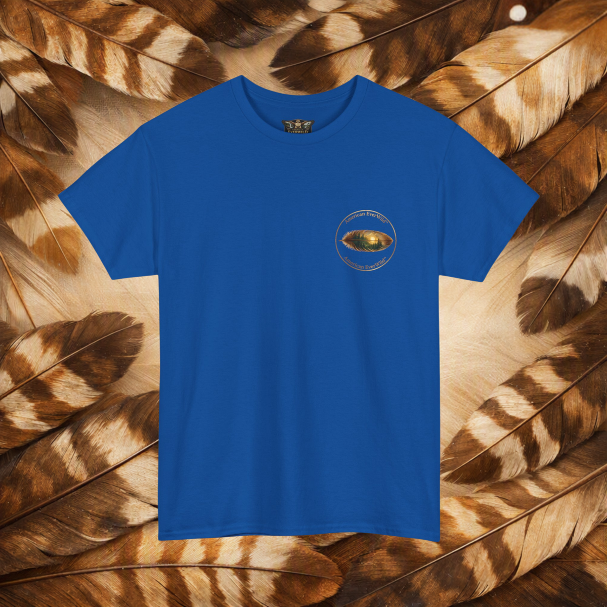 A royal blue short-sleeve crewneck t-shirt with a small circular American EverWild name top and bottom with a painted feather, displayed flat against a background of brown and beige feathers.