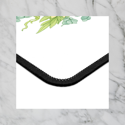 Square mouse pad corner with black textured edge and green floral leaves on white