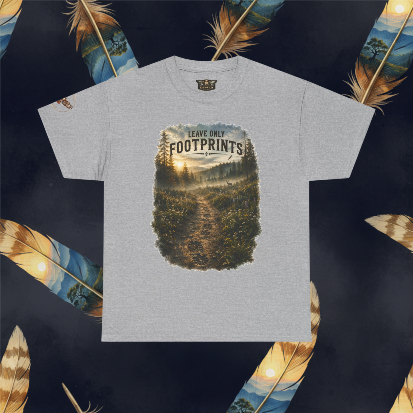A light gray heather crewneck t-shirt featuring a large rectangular graphic print of a forest trail with the text 'LEAVE ONLY FOOTPRINTS'. The t-shirt is displayed flat against a dark background decorated with large, colorful feathers.