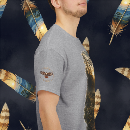 A man wearing a heather gray t-shirt with a graphic print of a hawk circle emblem with "American EverWild" and a vertical feather design, shown from a side profile against a dark patterned background with feathers.