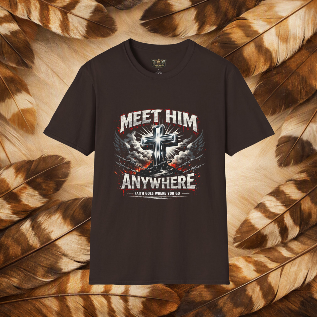 A dark brown graphic t-shirt displayed flat against a background of brown and beige feathers. The t-shirt features a graphic print with a metallic cross, wings, and the text 'MEET HIM ANYWHERE' in white and red.