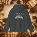A charcoal hoodie shown from the back, featuring a white graphic of mountains, trees, and a road with the text 'RAISED ON BACKROADS'. The hoodie is displayed flat against a background of brown and beige feathers.