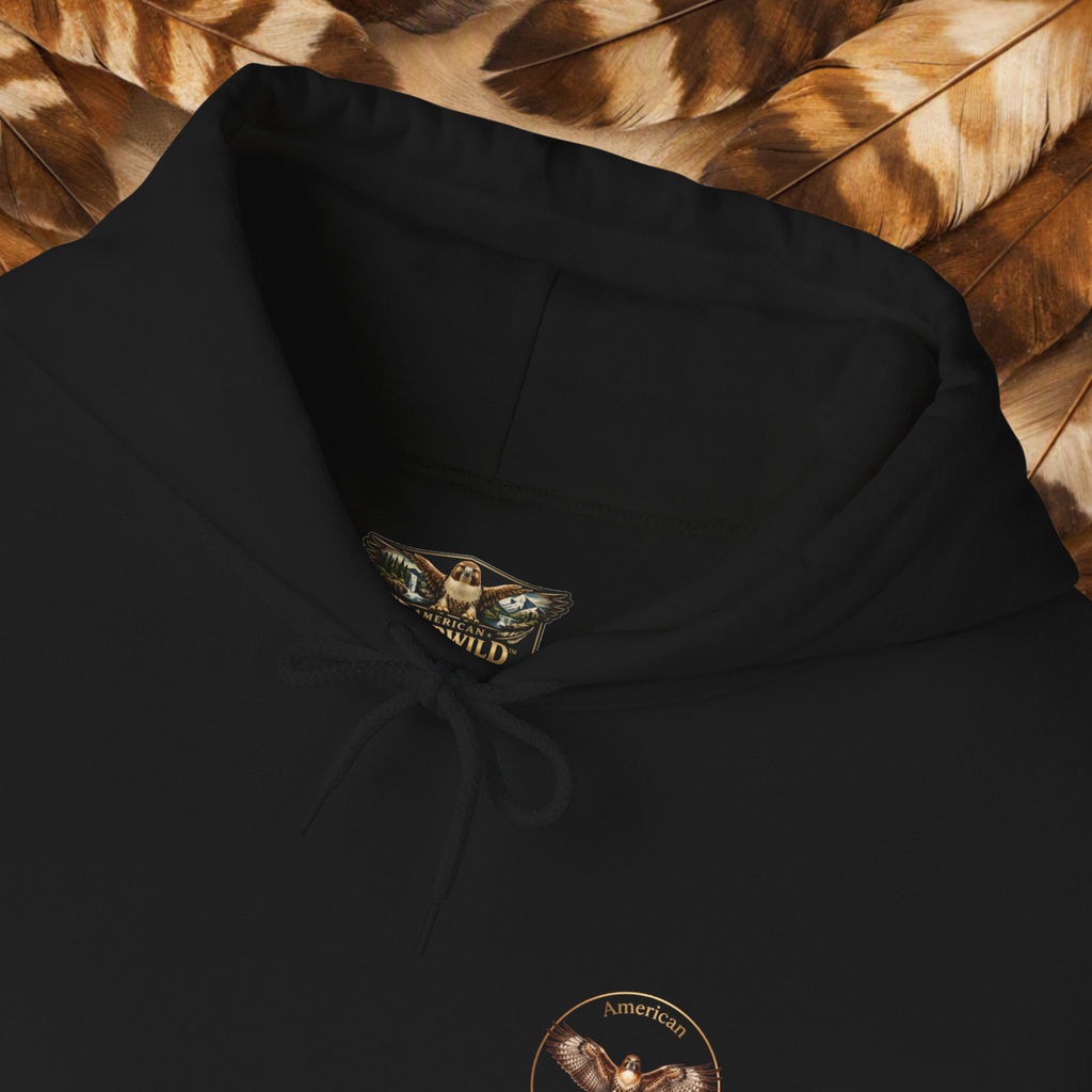A close-up of a black hoodie laid flat on a bed of brown feathers. The hoodie features a drawstring hood and a circular chest graphic showing a red-tailed hawk with the text 'AMERICAN EVERWILD.'