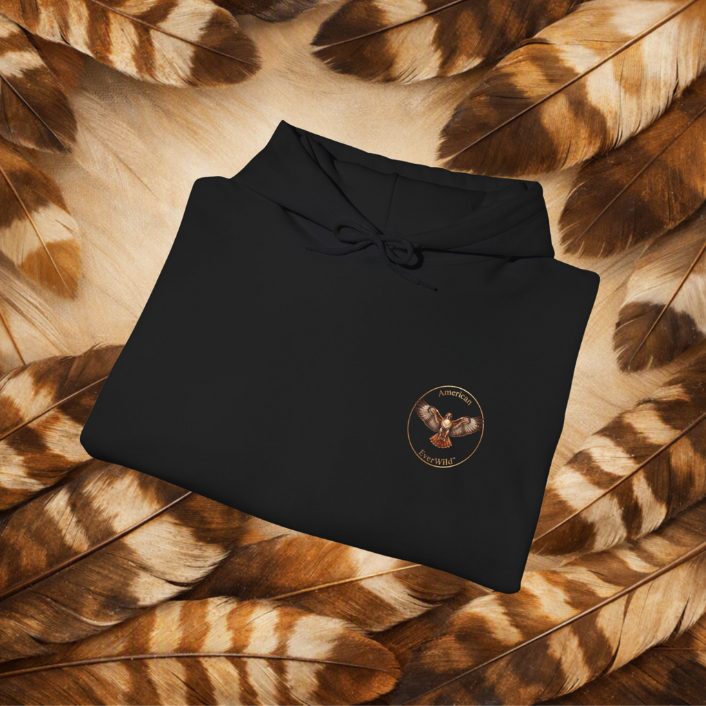 A folded black hoodie with a drawstring hood and a circular chest graphic for American EverWild, placed on a bed of brown and beige feathers. The graphic shows a red-tailed hawk