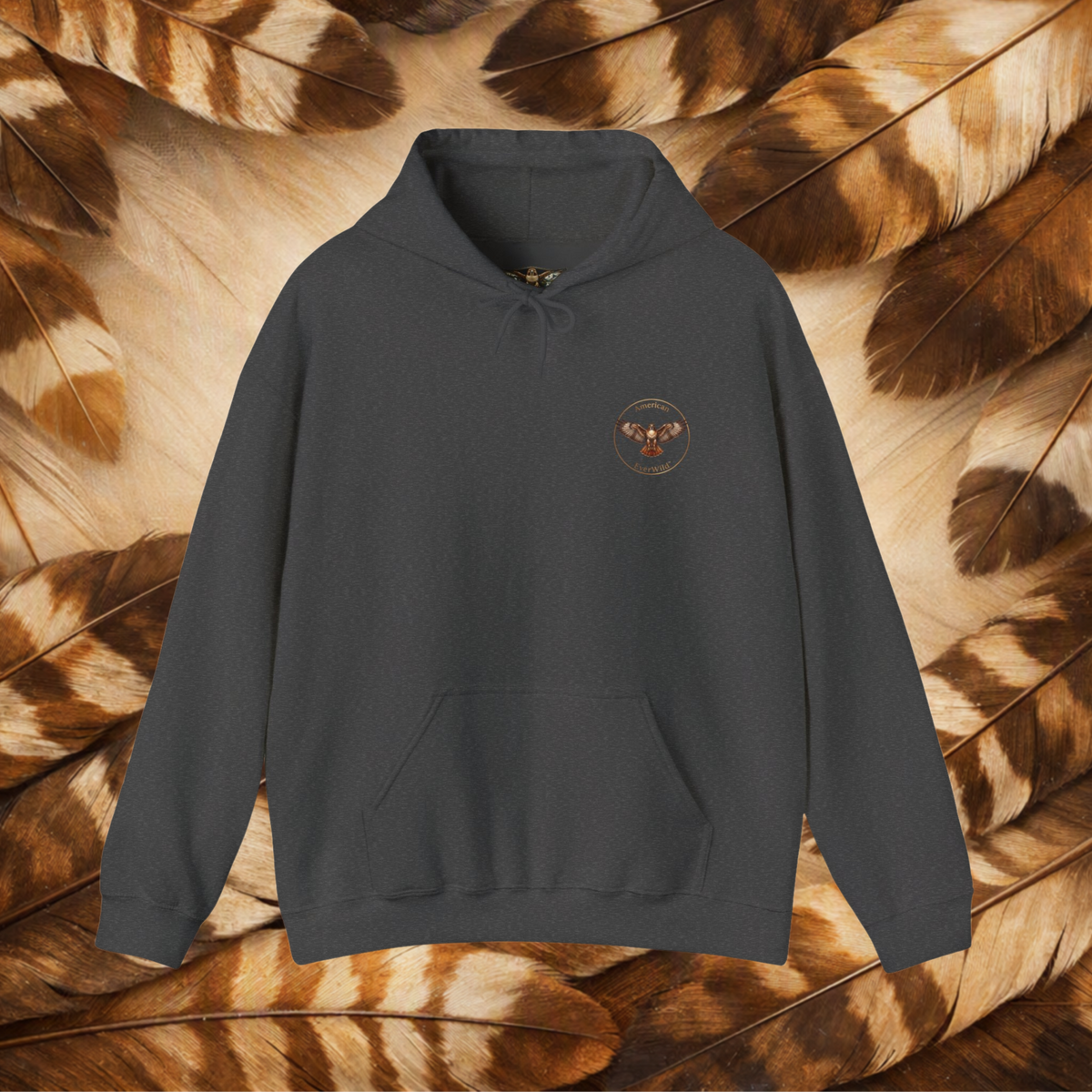 A dark charcoal gray pullover hoodie with a small circular embroidered logo for American EverWild on the left chest, displayed against a background of brown and beige feathers.