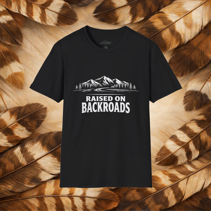 A black short-sleeve t-shirt with a white graphic print of mountains and the text 'RAISED ON BACKROADS' displayed against a background of brown and beige feathers.