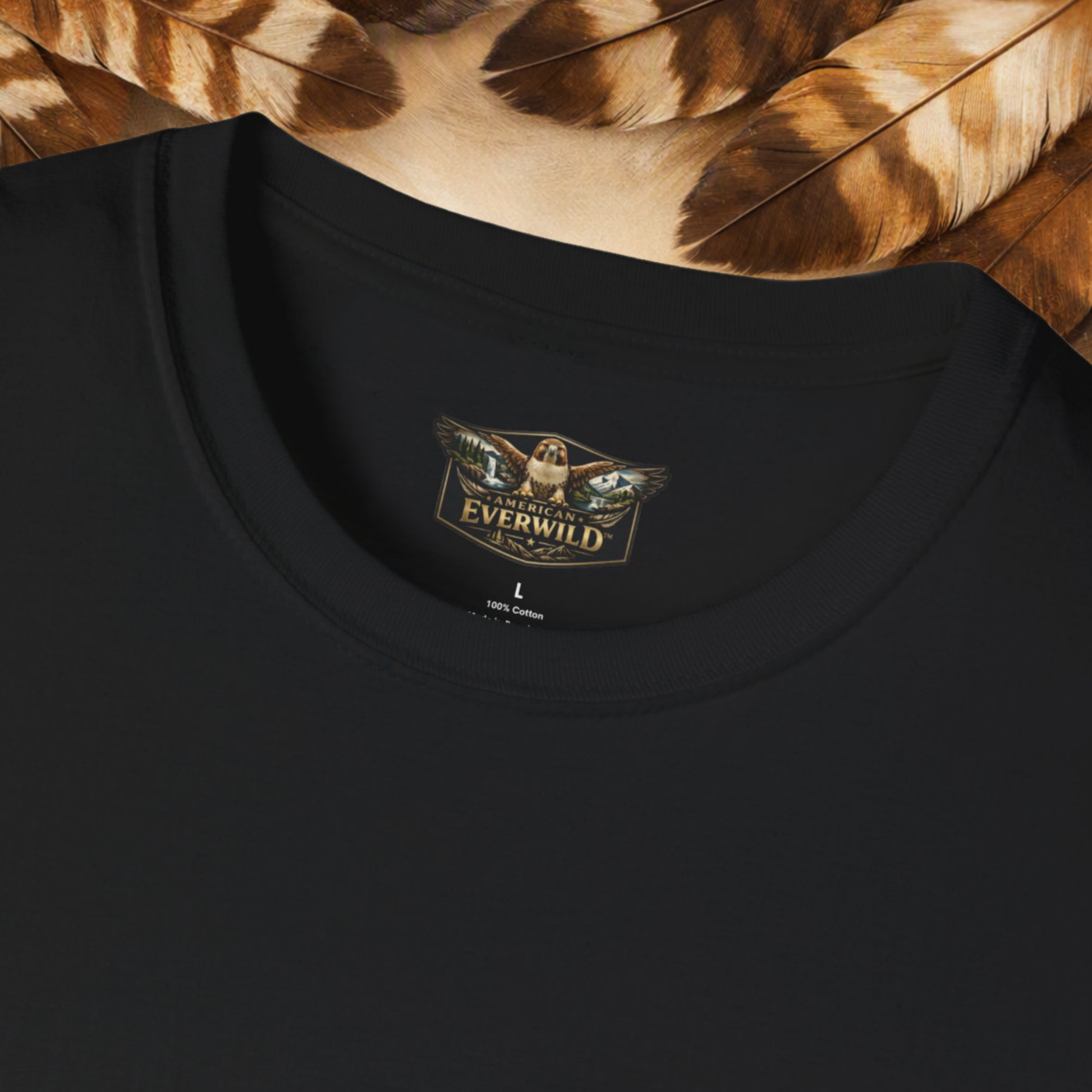 Close-up of a black crewneck t-shirt with a gold and brown 'American Everwild' hawk with painted wings logo printed inside the collar, styled with brown feathers at the top.