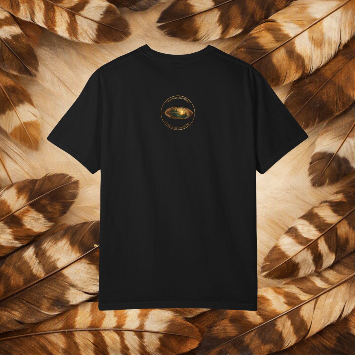 A black short-sleeve t-shirt in a circular emblem with a painted feather with "American EverWild", displayed flat against a background of brown and beige feathers.