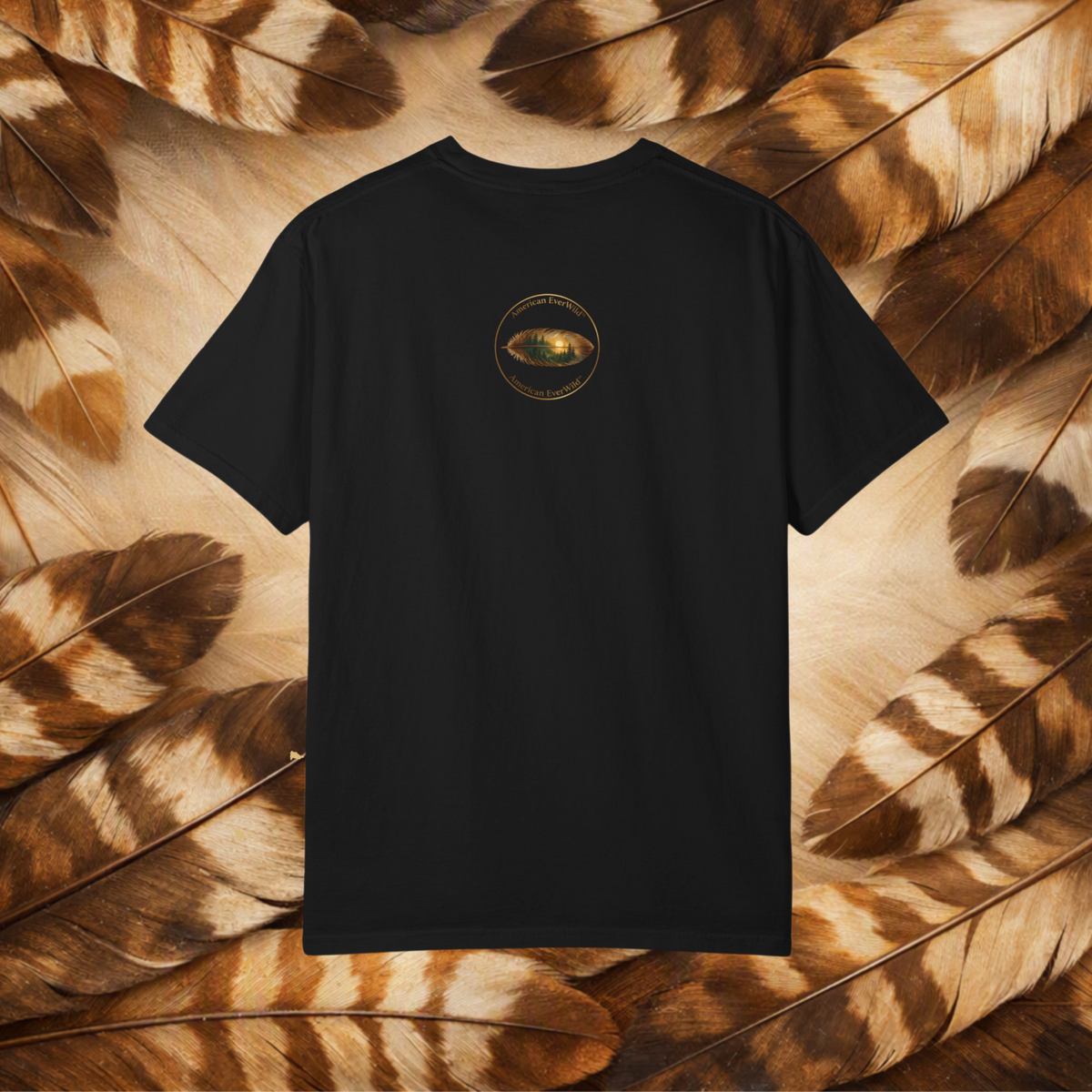 A black short-sleeve t-shirt in a circular emblem with a painted feather with "American EverWild", displayed flat against a background of brown and beige feathers.