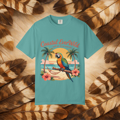 A turquoise short-sleeve t-shirt with a colorful graphic of a parrot on a beach and the text 'Coastal EverWild', presented flat against a background of brown and tan feathers.