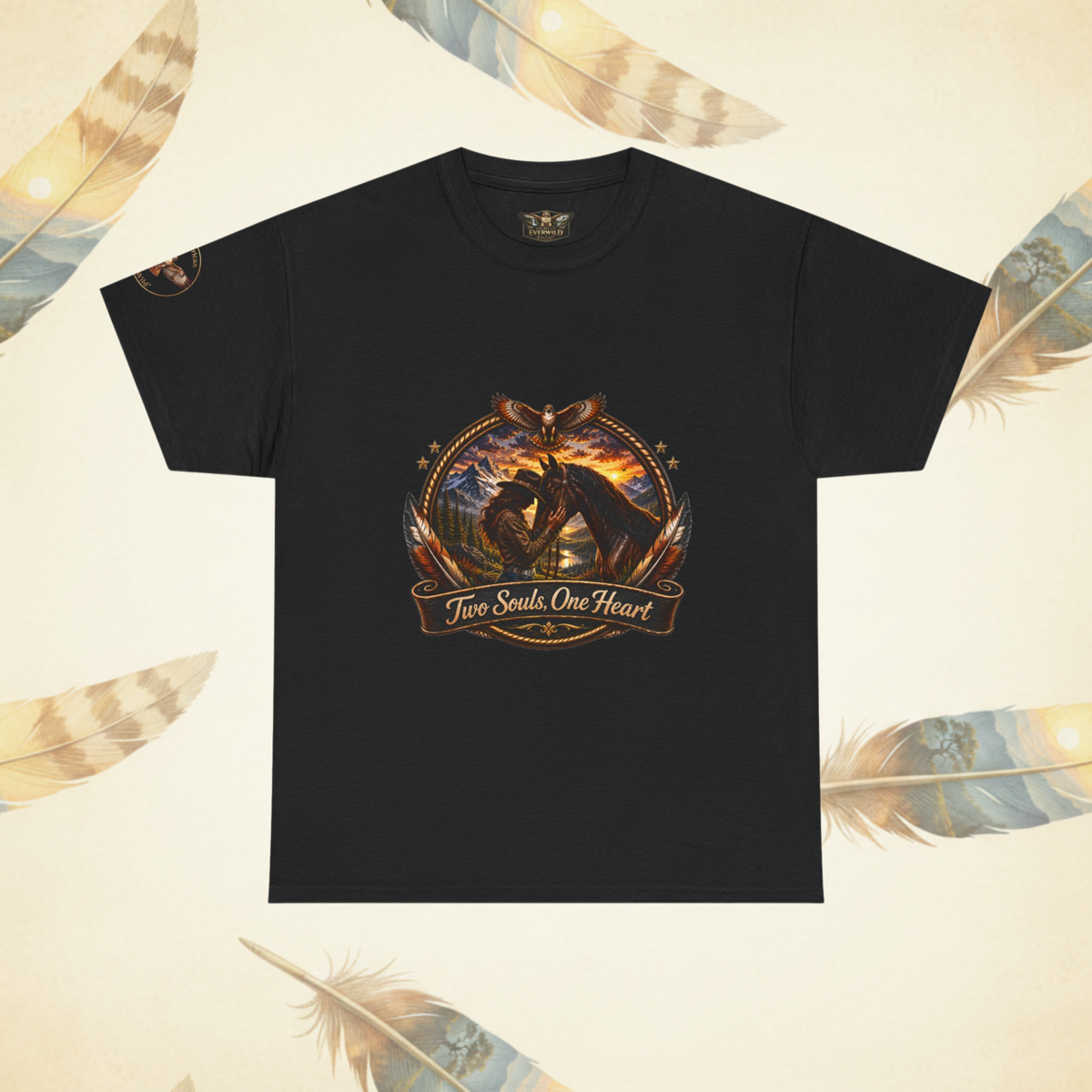 A black short-sleeve t-shirt with a detailed graphic on the chest showing a cowgirl and her horse at sunset with the text 'Two Souls One Heart'. The shirt is displayed flat against a cream-colored background decorated with stylized feathers.