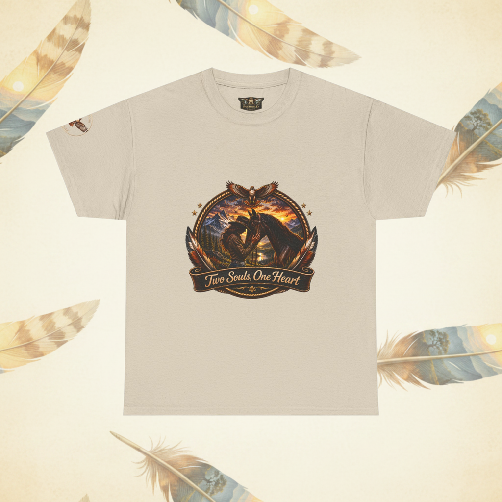 Asand colored crewneck t-shirt with a detailed graphic on the chest showing a cowgirl and her horse against a sunset, with the text 'Two Souls One Heart' on a banner below. The shirt is displayed flat against a cream-colored background decorated with feather illustrations.