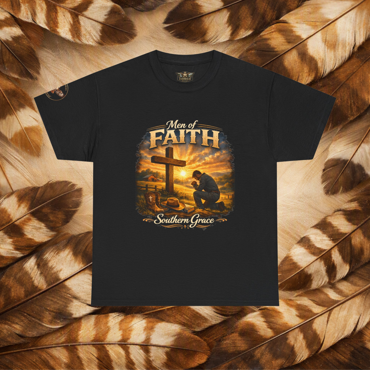 A black short-sleeve graphic t-shirt featuring a 'Men of Faith Southern Grace' Christian print with a cross and kneeling figure, displayed flat against a background of brown and beige feathers.
