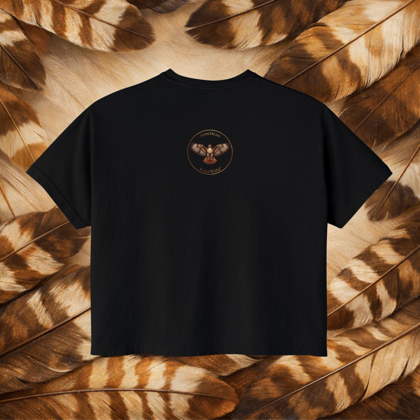 A black short-sleeve t-shirt with a circular graphic featuring a red-tailed hawk and the text 'American EverWild', presented flat against a background of brown and beige feathers.