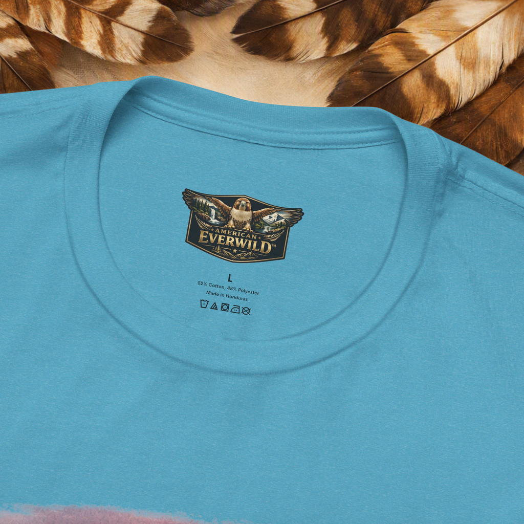 A close-up of a light blue crewneck t-shirt laid flat on a background of brown and beige feathers. The inside of the collar features a printed graphic logo for 'American EverWild' with a red-tailed hawk with painted wings.