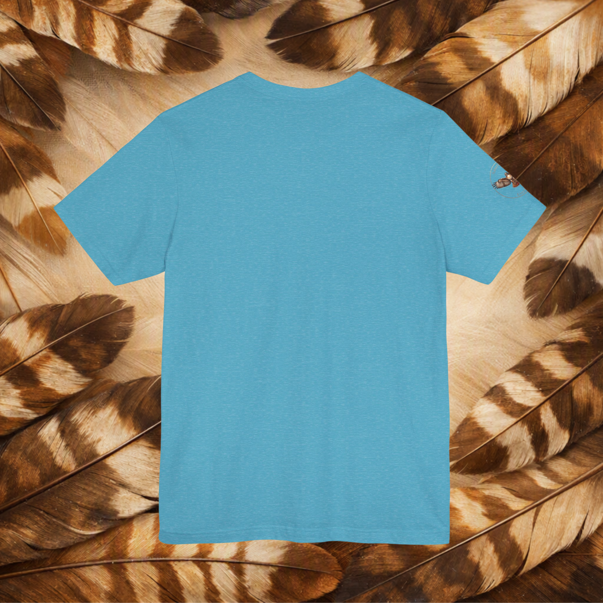 A blue tee shown from the back, the tee is laid flat on a background composed of brown and tan feathers.