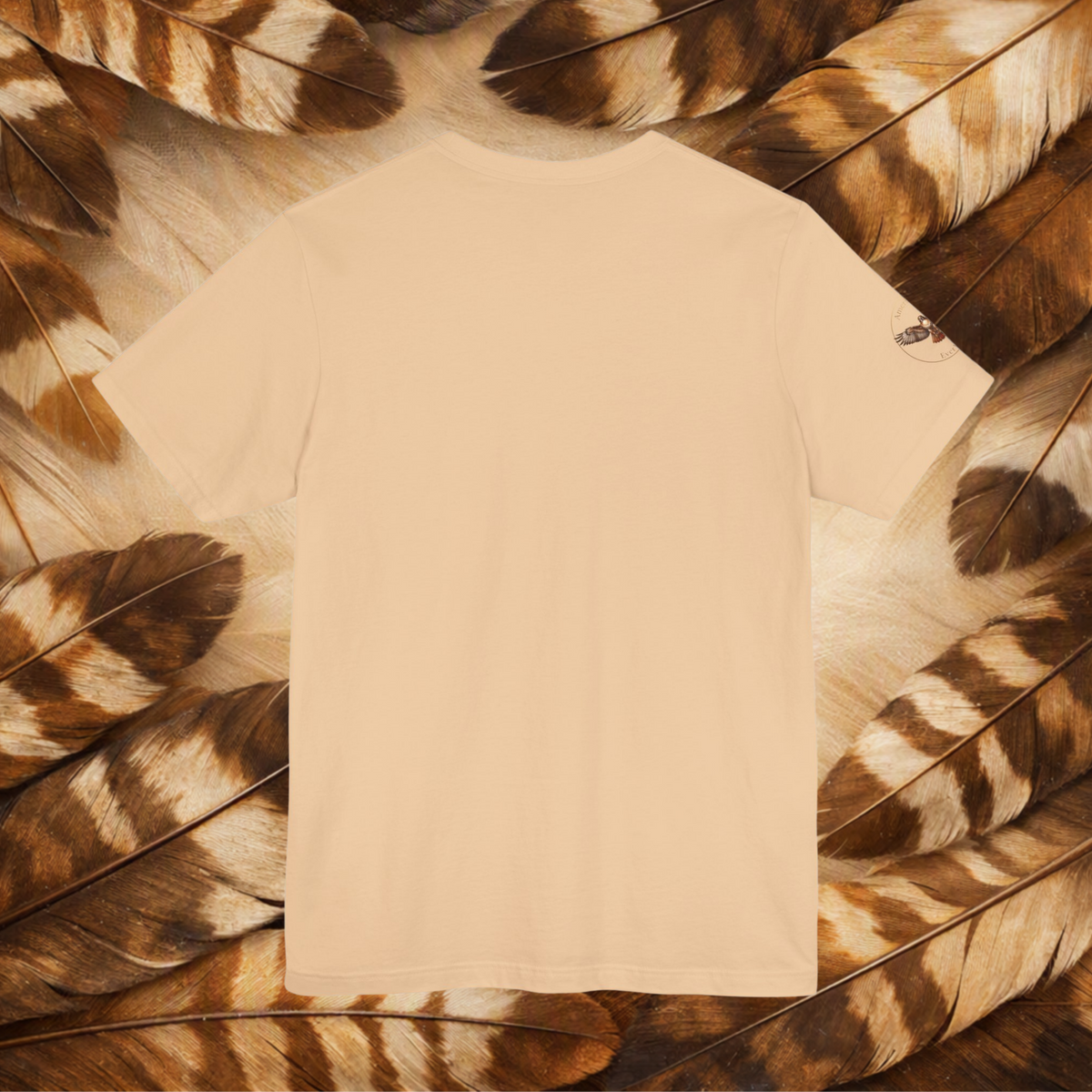 A close-up of a sand color tee laid flat on a bed of brown feathers. 