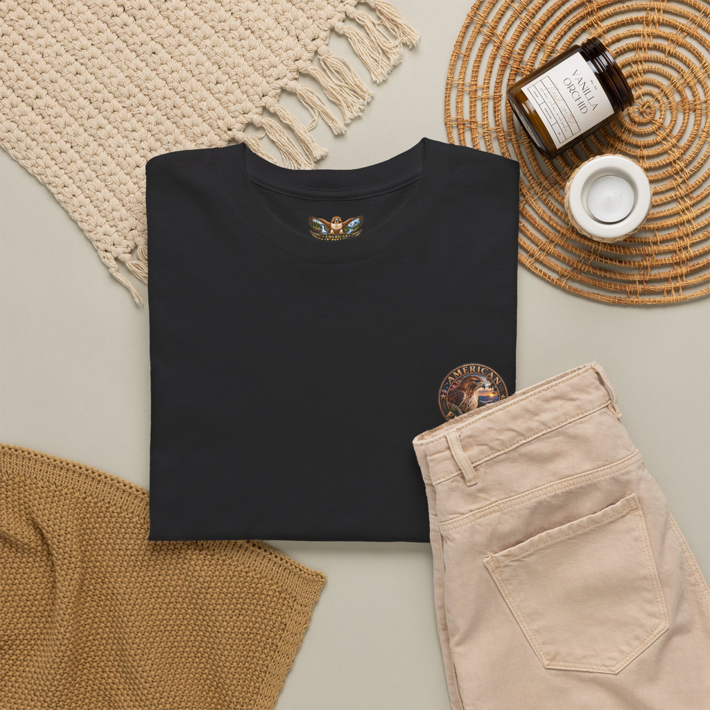 Black t-shirt with a "American EverWild" logo design on a neutral surface with beige pants and decorative items.