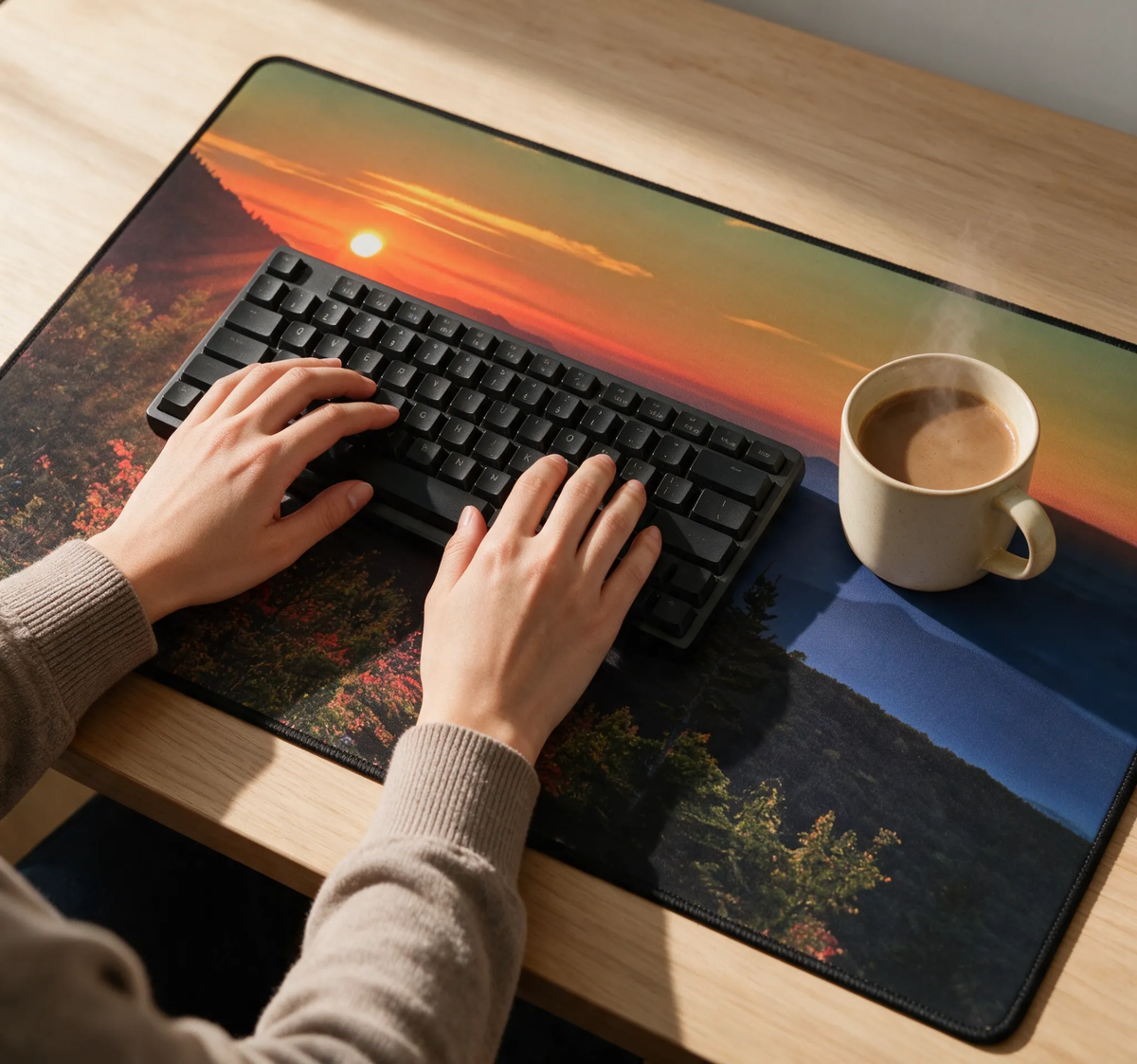 Extended desk mat under hands typing on black keyboard; sunrise mountain scene